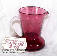 A small Pilgrim's mid century style cranberry creamer with an applied clear glass handle and has the original hang tag