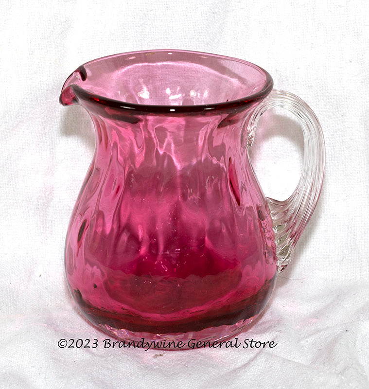 A small Pilgrim's mid century style cranberry creamer with an applied clear glass handle.