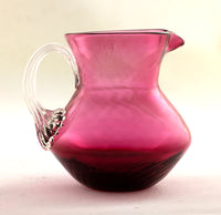 A Pilgrim's hand blown glass cranberry small pitcher with clear applied handle
